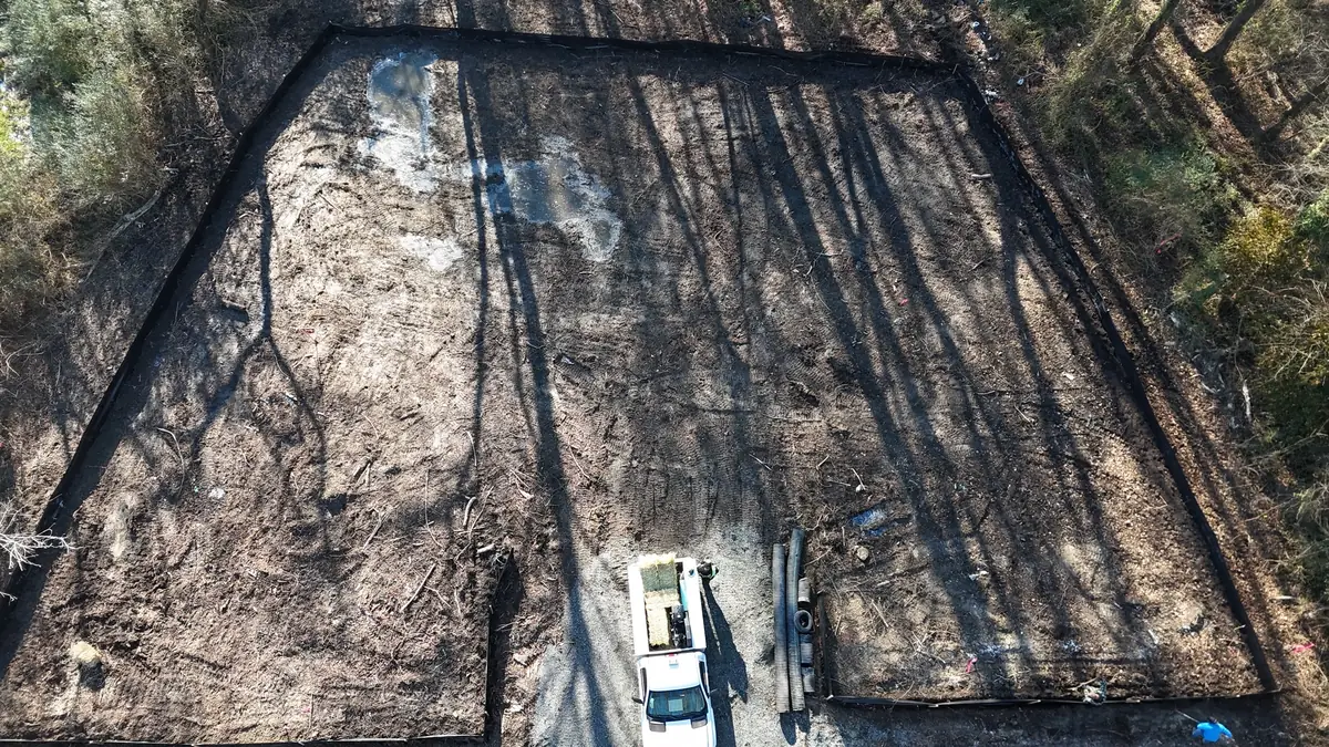 Aerial view of black silt fence around a cleared lot, with a pickup truck on the gravel drive