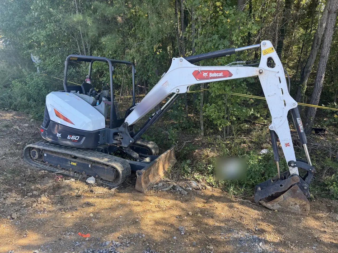 Compact excavator at the edge of a wooded lot